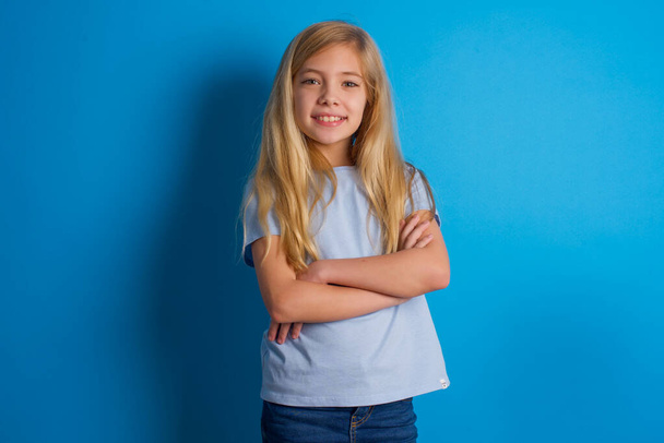 όμορφη καυκάσιος κορίτσι φορώντας μπλε t-shirt l είναι χαρούμενος χαμογελώντας και σταυρωμένα χέρια κοιτάζοντας με αυτοπεποίθηση στην κάμερα. Θετικό και με αυτοπεποίθηση άτομο. - Φωτογραφία, εικόνα