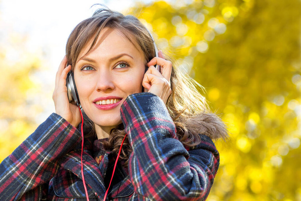 Beautiful autumn woman in autumn yellow street listening music, making selfie, being online - Фото, изображение