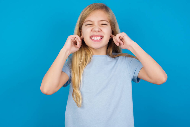 Stop making this annoying sound! Unhappy stressed out  beautiful caucasian girl wearing blue t-shirt   making worry face, plugging ears with fingers, irritated with loud noise. - Zdjęcie, obraz