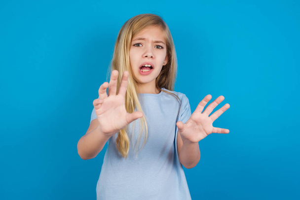 Dissatisfied  beautiful caucasian girl wearing blue t-shirt   frowns face, has disgusting expression, shows tongue, expresses non compliance, irritated with somebody. - Foto, Bild