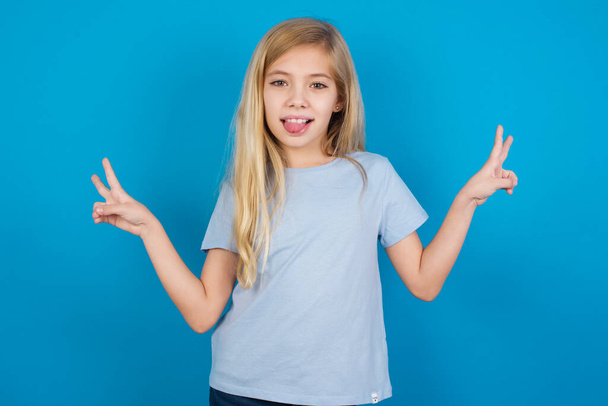 beautiful caucasian girl wearing t-shirt    with optimistic smile, showing peace or victory gesture with both hands, looking friendly. V signs. - Foto, Bild