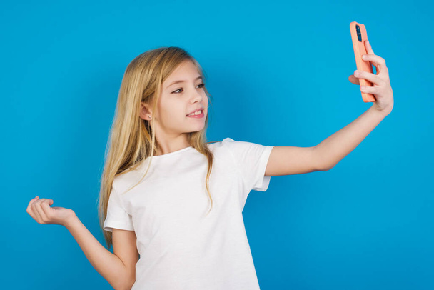 Muotokuva kauniista valkoihoisesta tytöstä t-paidassa ottamassa selfietä lähettääkseen sen ystäville ja seuraajille tai julkaistakseen sen sosiaalisessa mediassaan.. - Valokuva, kuva
