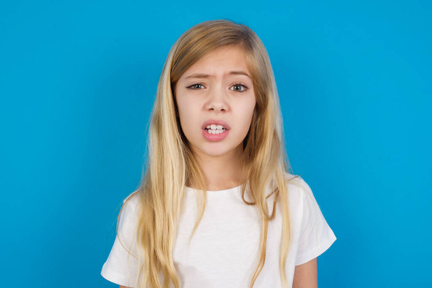 Portrait of dissatisfied beautiful caucasian girl wearing t-shirt   smirks face, purses lips and looks with annoyance at camera, discontent hearing something unpleasant - Photo, Image