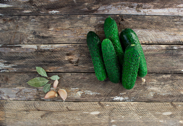 Verse komkommers met knoflook en laurierbladeren op een houten ondergrond. Pickles-beitsconcept - Foto, afbeelding