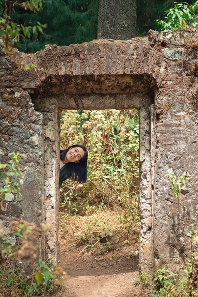 Girl smiling in forest, young woman smiling at door ruin in forest, outdoor travel concept - Photo, Image