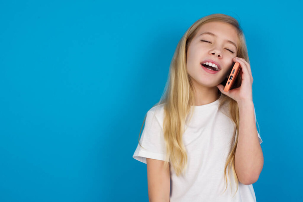Смішна красива біла дівчина в футболці сміється щасливо, має телефонну розмову, розважається другом, закриває очі. - Фото, зображення