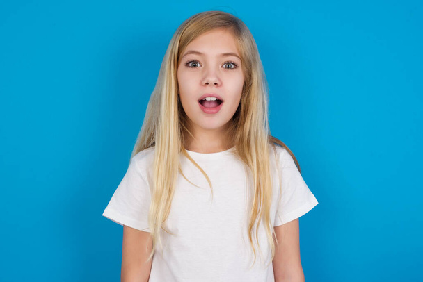 Shocked   beautiful caucasian girl wearing t-shirt   stares bugged eyes keeps mouth opened has surprised expression. Omg concept - Фото, зображення