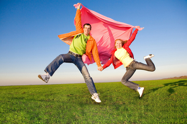 Joyeux jeune couple sautant dans le ciel au-dessus d'une prairie verte
 - Photo, image
