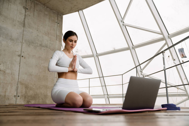 Young white woman using laptop during yoga practice indoors - Fotó, kép
