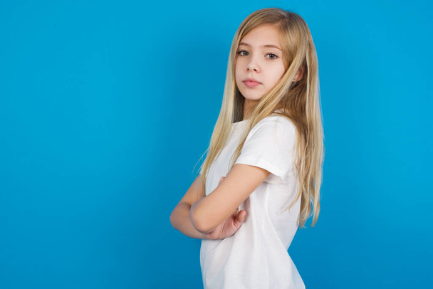 красива біла маленька дівчинка з довгим світлим волоссям у білій футболці на синьому фоні  - Фото, зображення