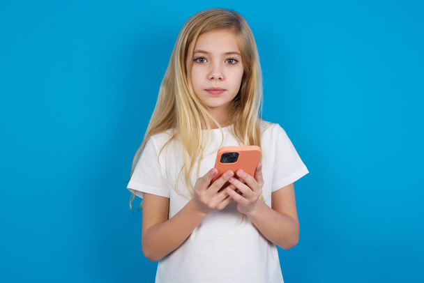 Portrait of serious confident  beautiful caucasian girl wearing t-shirt  holding phone in two hands - Fotografie, Obrázek