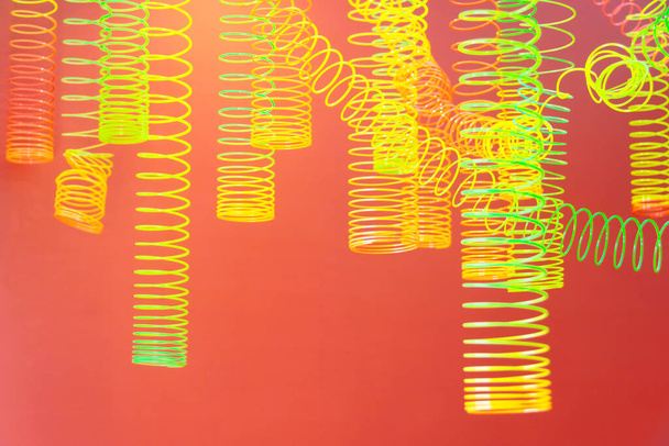 Περίληψη της σπείρα ουράνιο τόξο κρέμονται χρωματιστά παιχνίδια, κίτρινο ανοιχτό πράσινο σε ένα κόκκινο-πορτοκαλί φόντο - Φωτογραφία, εικόνα