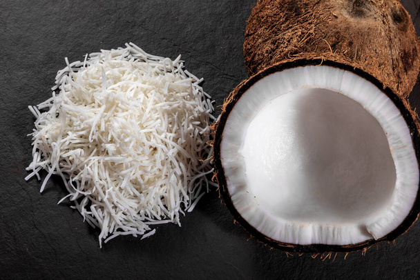 Otwarte orzechy kokosowe w środku na szczycie kamienia z wiórami kokosowymi i tartym orzechem kokosowym. - Zdjęcie, obraz