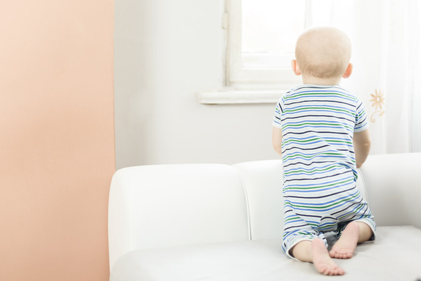 маленька дитина на колінах на дивані і дивиться у вікно
 - Фото, зображення