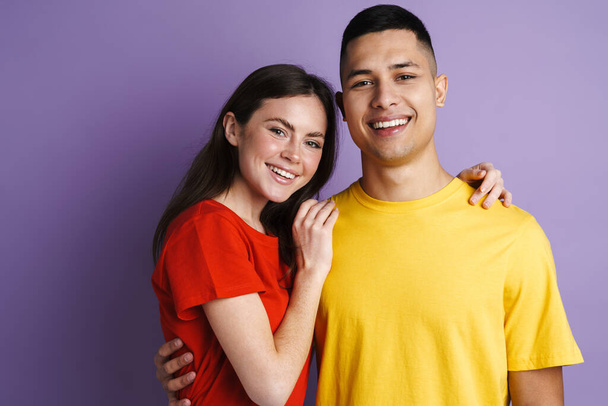 Brunette happy couple hugging and smiling at camera isolated over purple wall - Zdjęcie, obraz