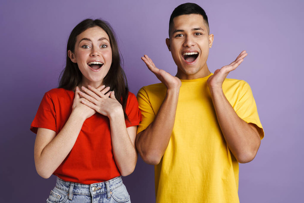 Brunette excited couple exclaiming and gesturing at camera isolated over purple wall - Фото, изображение