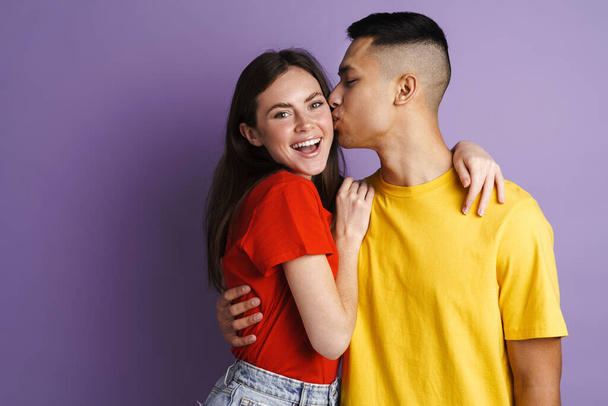 Brunette happy couple hugging and kissing at camera isolated over purple wall - Foto, afbeelding