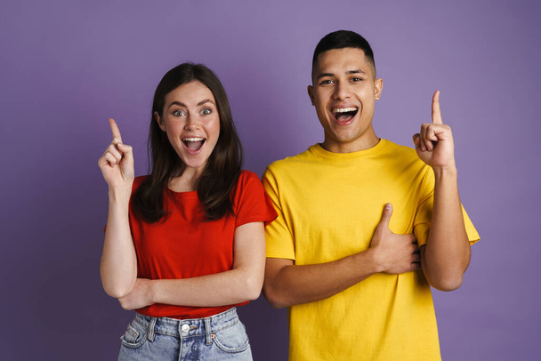 Brunette excited couple exclaiming and pointing finger upward isolated over purple wall - Foto, immagini