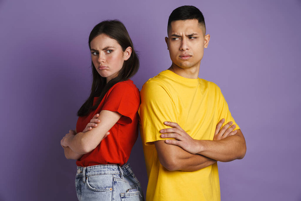 Resentful beautiful couple posing with arms crossed isolated over violet background - Фото, изображение