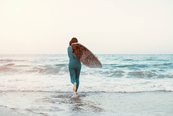 砂浜でボードで歩くサーファーの女の子。女性をサーフィン。ビーチで美しい若い女性。ウォータースポーツ。健康的なアクティブライフスタイル。夏休み。エクストリームスポーツ. - 写真・画像