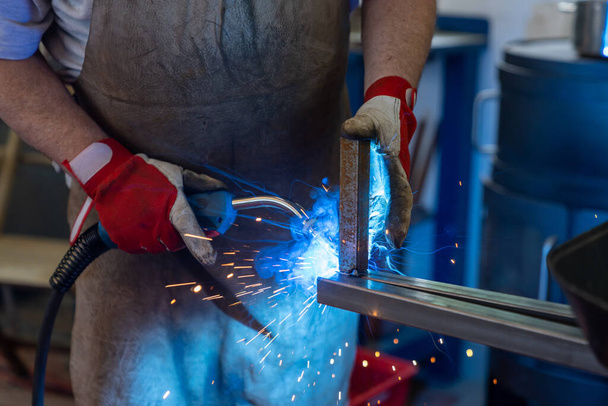 Detail eines Mannes, der Stahlrahmen in einer Werkstatt für Fälschung und Metallverarbeitung schweißt - Foto, Bild