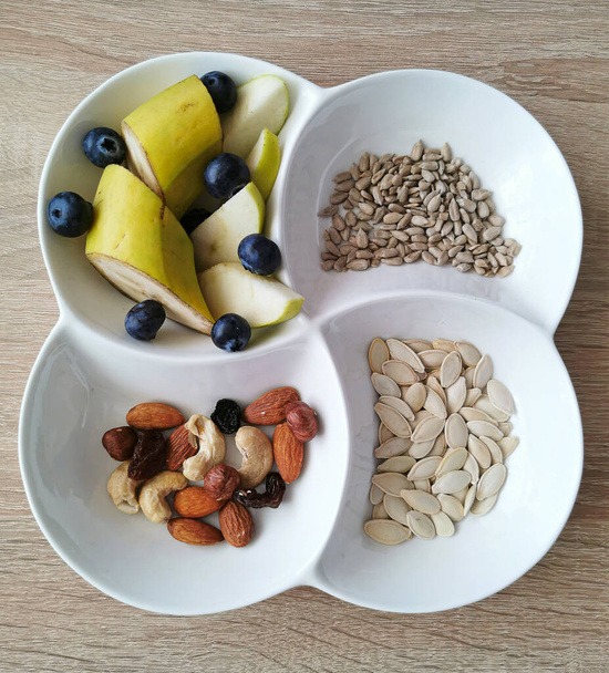 A healthy snack. Nuts, sunflower and pumpkin seeds. Banana pieces, apples and blueberries - Photo, Image