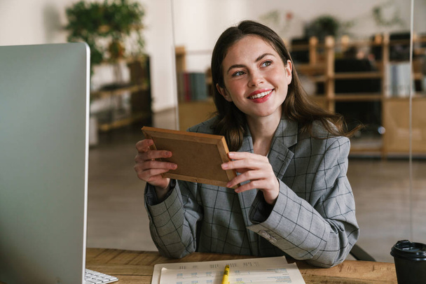 Young smiling woman looking at photo while working in office - Foto, Bild
