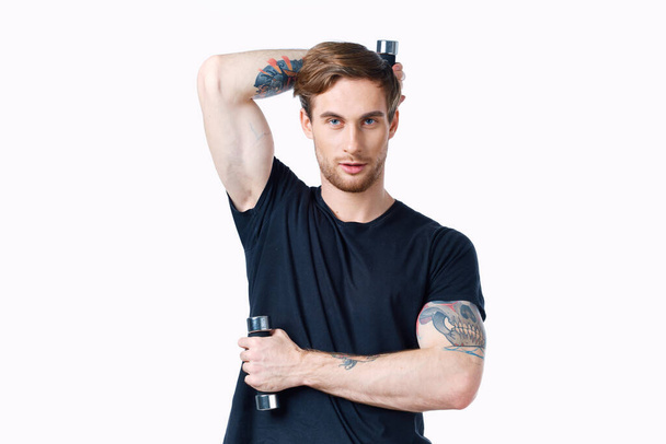tipo con mancuernas sostiene su mano detrás de su cabeza y fondo claro negro camiseta deporte fitness - Foto, imagen
