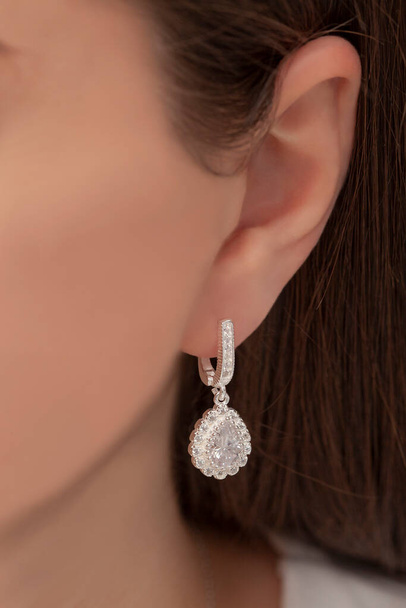 Zilveren hangende oorbellen bevestigd aan het oor van een geprepareerde dame. Sieraden afbeelding die kan worden gebruikt in e-commerce verkoop. - Foto, afbeelding