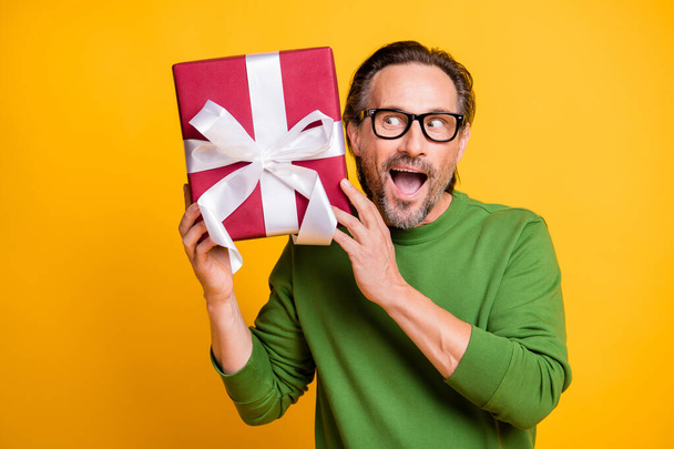 Photo portrait of man in glasses looking interested on gift box wrapped with ribbon isolated vibrant yellow color background - Fotó, kép