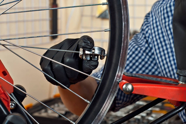 Bicycle lunch close up. Bicycle maintenance and service. Wheel rim alignment tool. A gloved man aligns the spokes of a bicycle. - 写真・画像