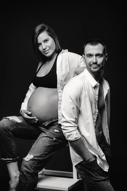 a pregnant woman and a man in a white shirt and jeans in a studio on a black background. - Foto, immagini