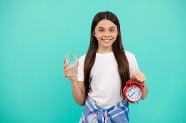 happy teen girl hold glass of water and alarm clock to stay hydrated and keep daily water balance in time, daily water. - Photo, Image