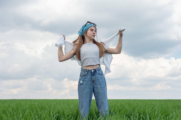 μοντέρνο μικρό κορίτσι έφηβος, σε ένα πεδίο από πράσινο γρασίδι, σε ένα φόντο συννεφιασμένο ουρανό. - Φωτογραφία, εικόνα