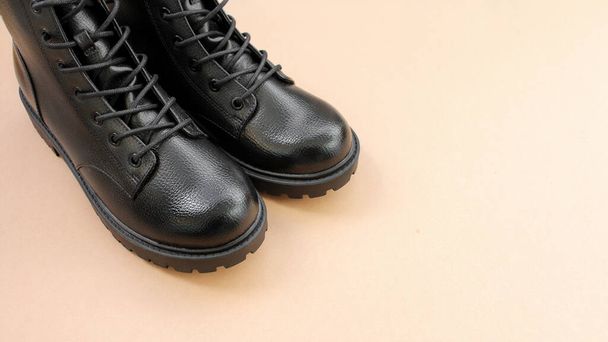 Zwarte leren laarzen op bruine achtergrond. Modieuze moderne vrouwelijke schoenen militaire stijl - Foto, afbeelding