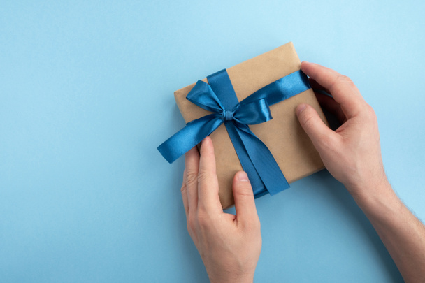 Подарочная коробка в руках мужчины на светло-голубом фоне. День отца, день рождения и праздничная концепция. Вид сверху, плоский, копировальное пространство - Фото, изображение