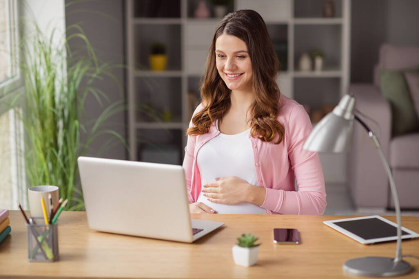 Portrait of lovely cheerful pregnant girl staying home self isolation watching web tutorial pastime house indoors - 写真・画像