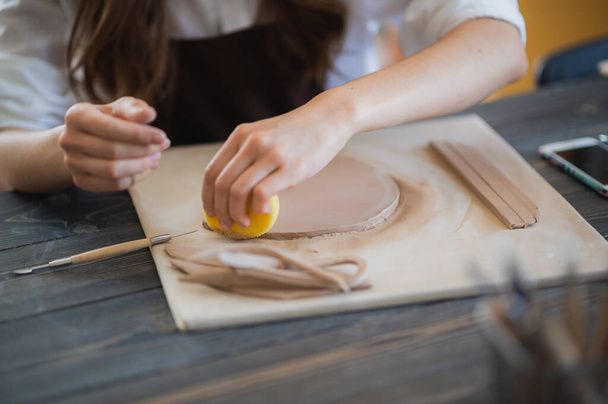Ремесленница-гончар готовит материал для своей керамики. Женские руки прикрепляют глиняную деталь к будущему керамическому изделию. Работать крупным планом. - Фото, изображение