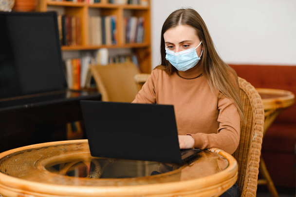 mladá dívka v modré lékařské masky práce v kavárně na notebooku - Fotografie, Obrázek