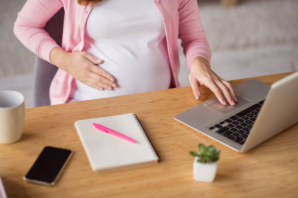Cropped view of attractive pregnant girl copywriter staying home working remotely typing e-mail caressing belly in flat house indoors - Foto, Bild