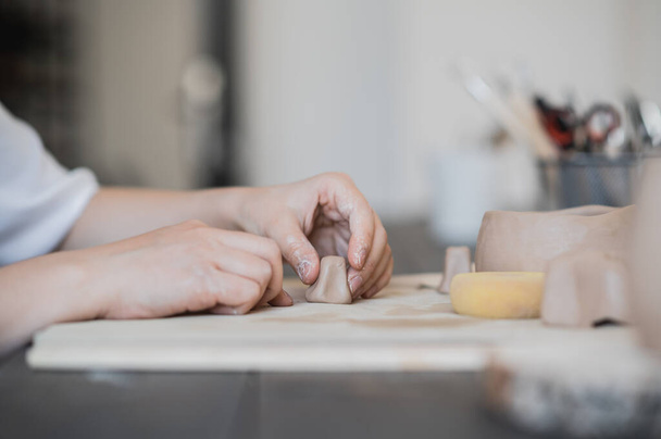 Ремесленные руки соединяют глиняные детали из сырой глины, мастерские пальцы работают с кусочками глины, женщины сидят в мастерской за столом - Фото, изображение