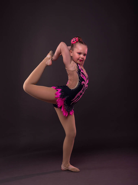 Graciosa niña tratando de hacer círculo en gimnasta negro y rosa traje en el estudio. - Foto, imagen