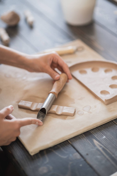 Ręce rzemieślnika łączą części gliniane wykonane z surowej gliny, palce mistrza pracują z kawałkami gliny, samica siedzi w warsztacie za stołem - Zdjęcie, obraz
