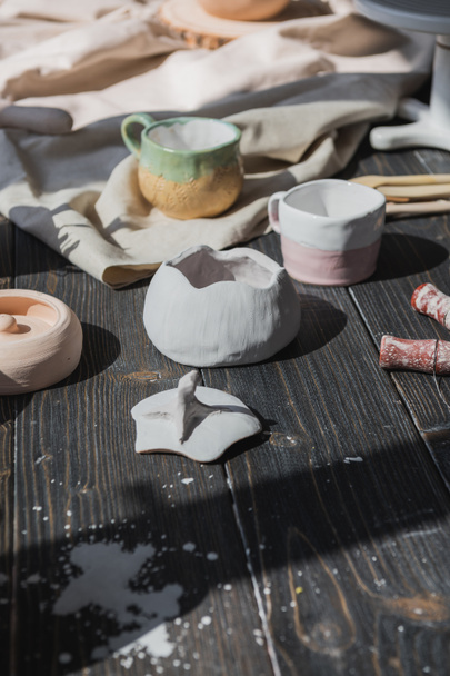 A close-up view of clay plates and a paint brush on a wooden table and dried flowers on a background. Crafted tableware in a pottery studio. Handmade ceramic. Pottery studio concept. - Фото, зображення