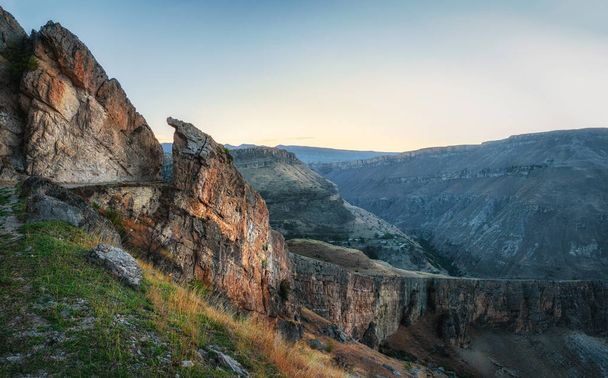 Kleurrijk ochtendlandschap met silhouetten van grote rotsachtige bergen en epische diepe kloof. Vuile bergweg, serpentine met een klif en een prachtig panoramisch uitzicht op de kloof. - Foto, afbeelding