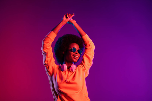 Photo of festive clubber lady enjoy dance raise hands wear hoodie headphones sunglass isolated gradient neon background - Фото, изображение