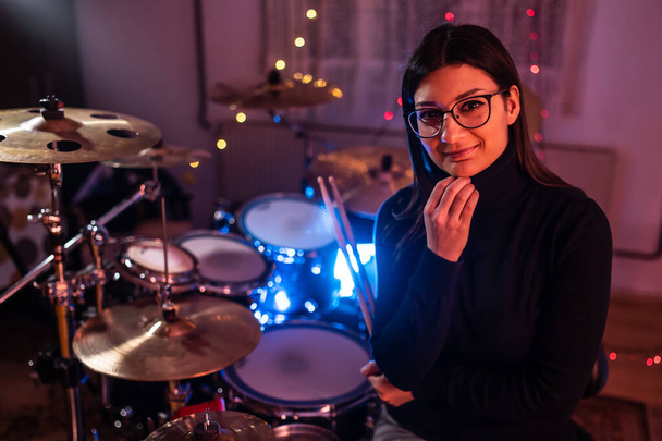 Vorderseite Porträt einer erwachsenen kaukasischen Frau, die vor Schlagzeug posiert, das in einem dunklen Raum oder Studio steht - Schlagzeugerin, die nachts zur Seite schaut - Kopierraum echte Menschen - Foto, Bild