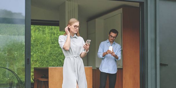 Casal bem sucedido de millennials em pé na casa moderna com smartphones - Foto, Imagem