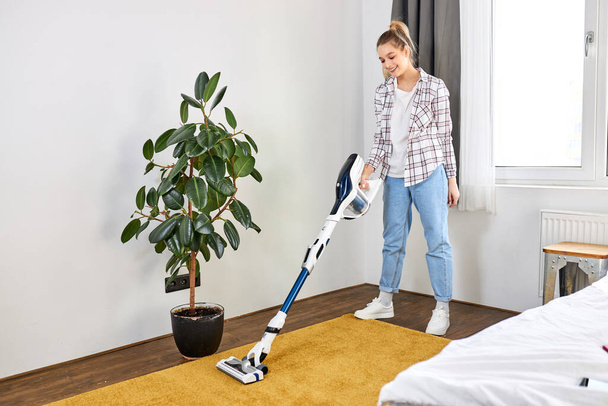 Woman in casual wear vacuum cleaning yellow carpet, tidying white modern living room. Home, housekeeping concept - Fotoğraf, Görsel