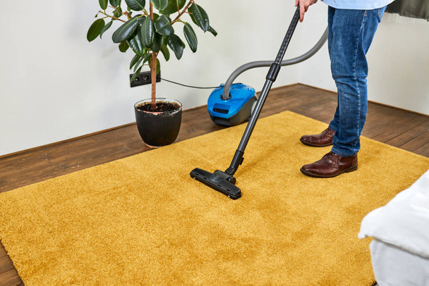 Cropped man cleaning floor carpet with vacuum cleaner in modern white living room - Valokuva, kuva